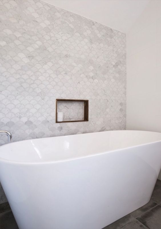 a serene bathing space with marble fish scale tiles, an oval tub, large scale tiles on the floor and a niche shelf