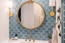 a sink space with a blue scallop tile accent wall, a neutral vanity, a round mirror, brass fixtures and cool wall lamps