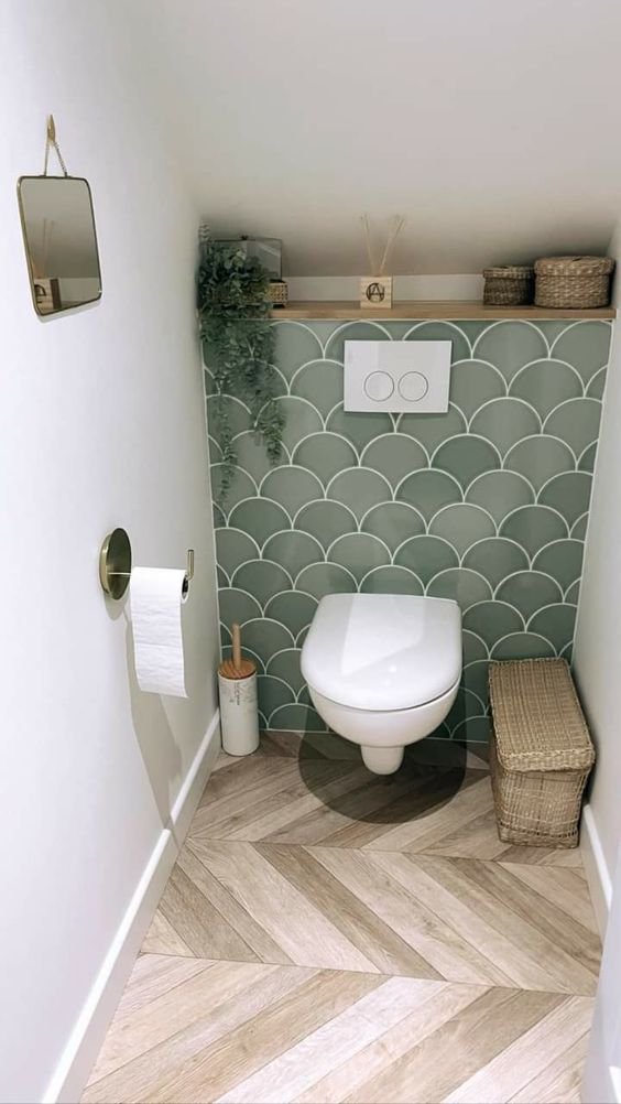 a small attic powder room with a green tile accent wall, a shelf and some baskets and a small mirror is cool