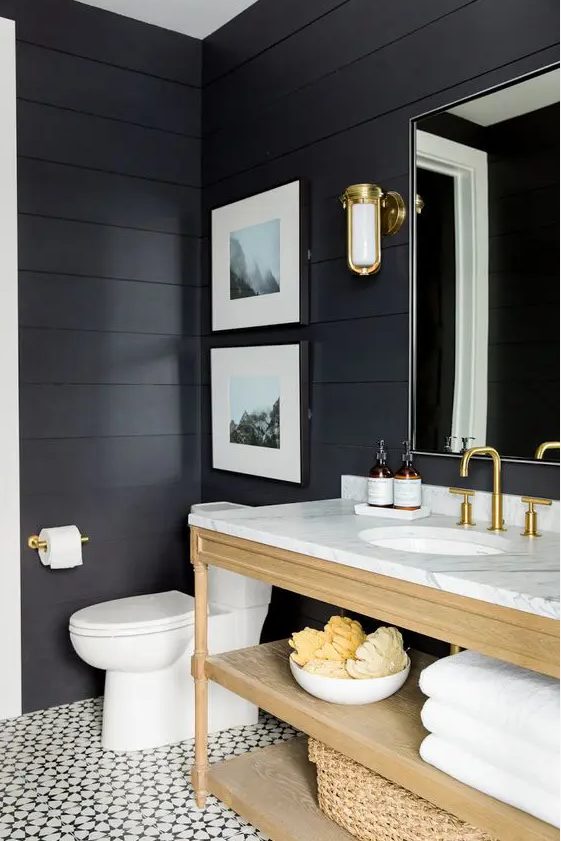 a soot bathroom with a light stained vanity and baskets, a mirror, sconces and a mini gallery wall is cool