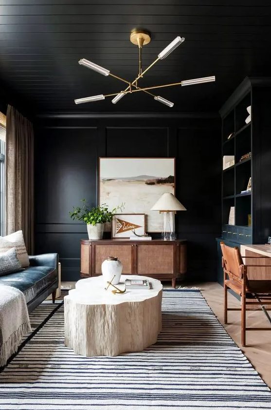 a soot home office with a black leather sofa, a stained credenza, a desk and a chair, a chandelier, a bleached stump table