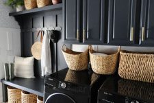 a soot laundry room with a rack and a bench, baskets for storage and black appliances is a cool and chic space