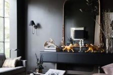 a soot living room with a black console and a chic mirror, blush chairs, a grey sofa, eye-catching coffee tables