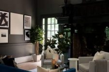 a soot living room with a dark-stained storage unit, creamy chairs, a navy sofa, a glass coffee table and potted plants