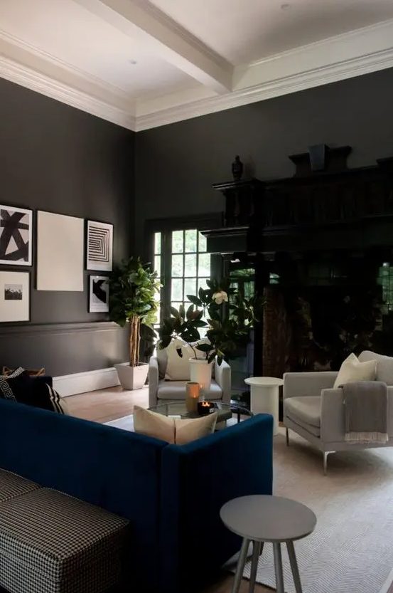 a soot living room with a dark stained storage unit, creamy chairs, a navy sofa, a glass coffee table and potted plants