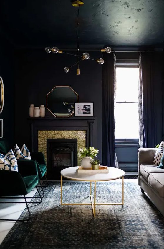 a soot living room with a fireplace clad with gold and soot panels, a neutral sofa, a coffee table, green chairs, a stylish chandelier
