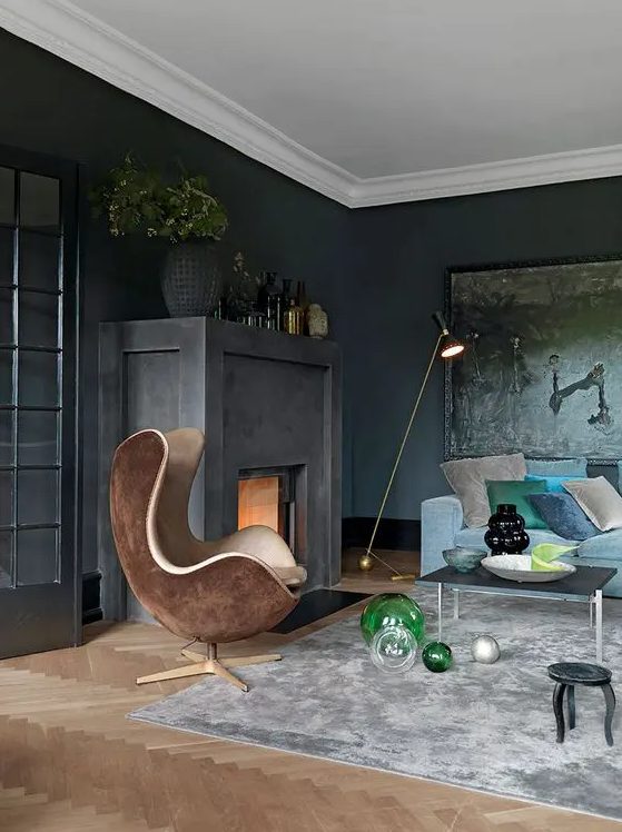 a soot living room with a firpelace, a dark artwork, a blue sofa and colorful pillows, a brown egg shaped chair and some vases
