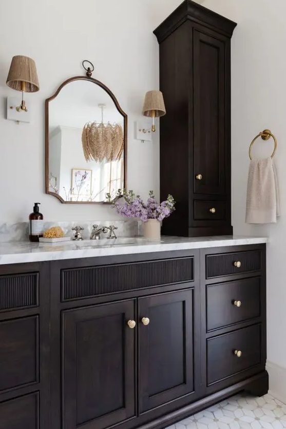 A sophisticated dark stained vanity with gold knobs, a vintage mirror and sconces create a very elegant and somewhat dramatic look