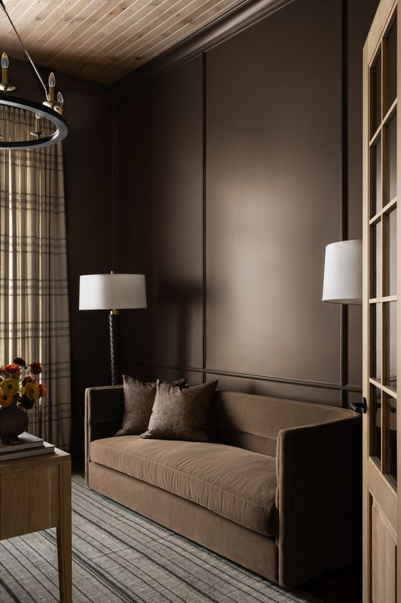 a sophisticated space with brown walls, a brown sofa with pillows, printed textiles and a large chandelier
