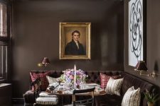 a sophisticated vintage dining room with chocolate brown walls, an aubergine tufted sofa, a table and chairs, some artwork