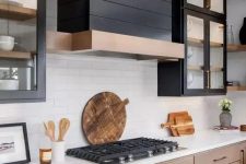 a stained wood kitchen with upper black glass cabinets, a black wood clad hood and white countertops