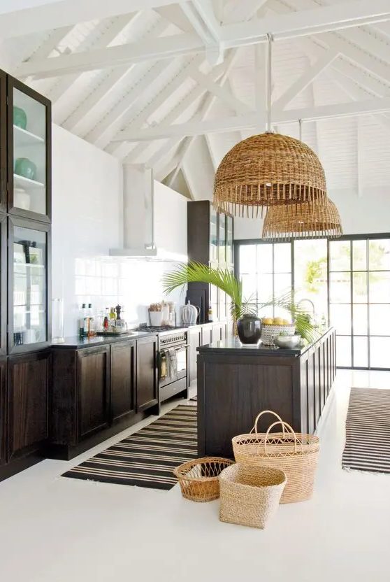 A stylish kitchen with dark stained cabinets and a large kitchen island, woven pendant lamps and greenery is amazing