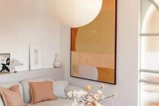 a stylish modern living room with a neutral sofa and peachy pillows, a statement artwork, a peachy rug and a glass coffee table