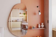 a stylish nook with a Peach Fuzz accent, built-in light, some shelves, a creatively shaped mirror and some decor