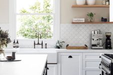 a stylish white farmhouse kitchen with a blck kitchen island, white stone countertops and a white scallop tile backsplash