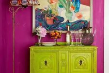 a super bold combo of a fuchsia wall and a chartreuse vintage cabinet, a bold artwork and a floor lamp