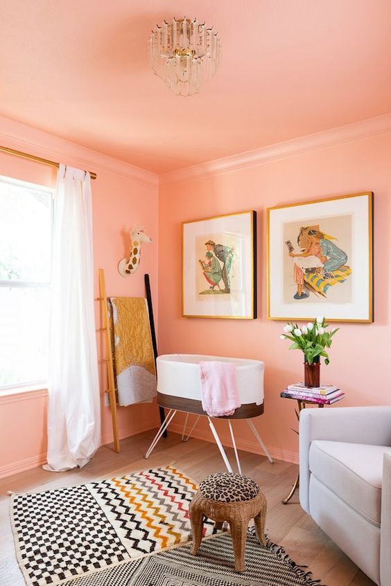 a sweet nursery with Peach Fuzz walls and a ceiling, a crib, a chair, a gallery wall and printed rugs