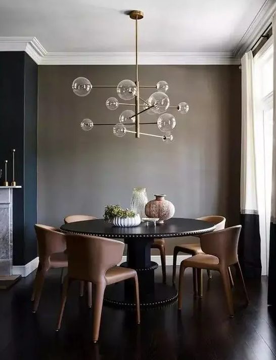 A taupe dining space wiht a large round table in black, chocolate colored leather chairs and a catchy bubble chandelier