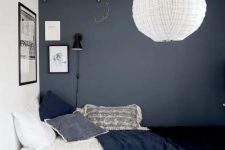 a teen bedroom with a graphite grey wall, an open shelf, a bed with navy bedding, a basket, a pendant lamp and a rug