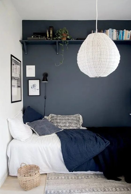 a teen bedroom with a graphite grey wall, an open shelf, a bed with navy bedding, a basket, a pendant lamp and a rug