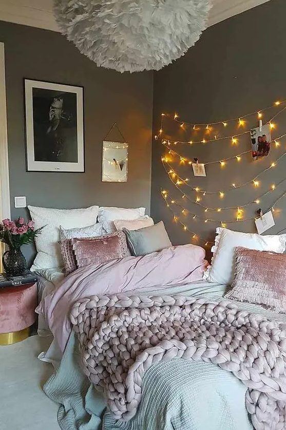 a teen bedroom with grey walls, a bed with grey and pink, string lights on the wall, a fluffy pendant lamp and blooms