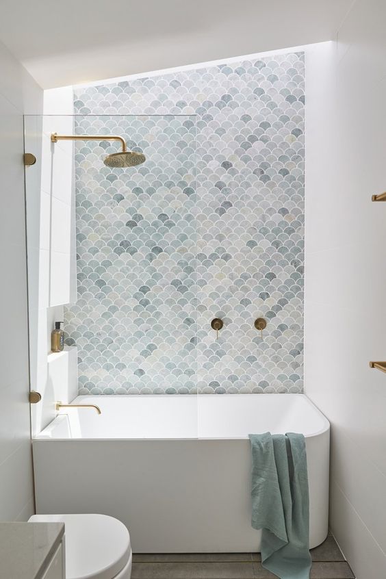 a tiny white bathroom with a light blue fish scale tile wall and white appliances plus brushed brass fixtures