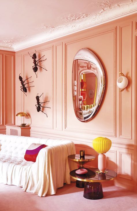 a unique living room with Peach Fuzz walls and giant ants as decor, a white tufted sofa, a mirror and some tables