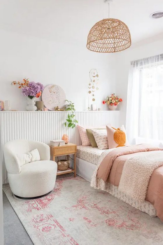 a vivacious teen girl bedroom in neutrals with a paneled shelf with blooms and art, a bed with printed bedding, a white chair and a woven pendant lamp