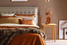a warm-colored earthy bedroom with a taupe accent wall, a grey bed with bright bedding, a stool with dried herbs and a pendant lamp