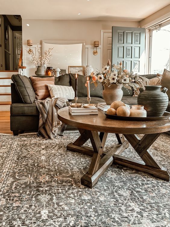 a welcoming earthy living room with a grey sofa and earhty pillows, a printed rug, a stained round table and some candles