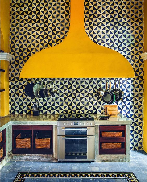a whimsical kitchen with open cabinets with baskets and a bold geo tile wall plus an oversized yellow hood that makes a statement