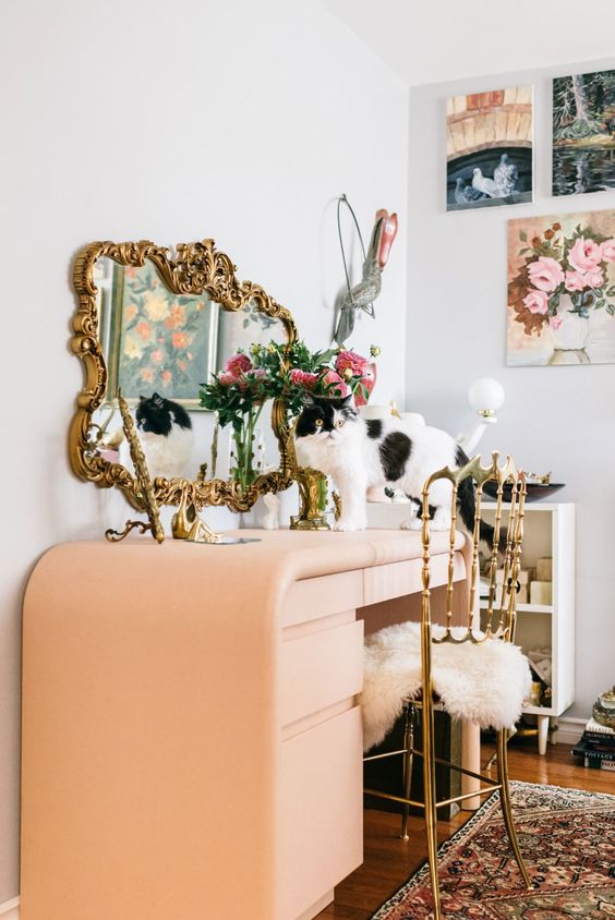 a whimsical makeup space with a Peach Fuzz vanity, a mirror in an ornated frame and a gallery wall