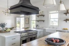 a white farmhouse kitchen with a stained kitchen island, an oversized black hood and pendant lamps