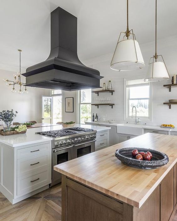 a white farmhouse kitchen with a stained kitchen island, an oversized black hood and pendant lamps