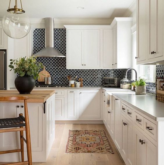a white farmhouse kitchen with shaker cabinets, a kitchen island with a butcherblock countertop, a black scallop tile backsplash and a boho rug