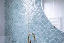 an accent wall done with blue fishscale tiles for an ocean feel in the bathroom, brass fixtures stand out in the backdrop