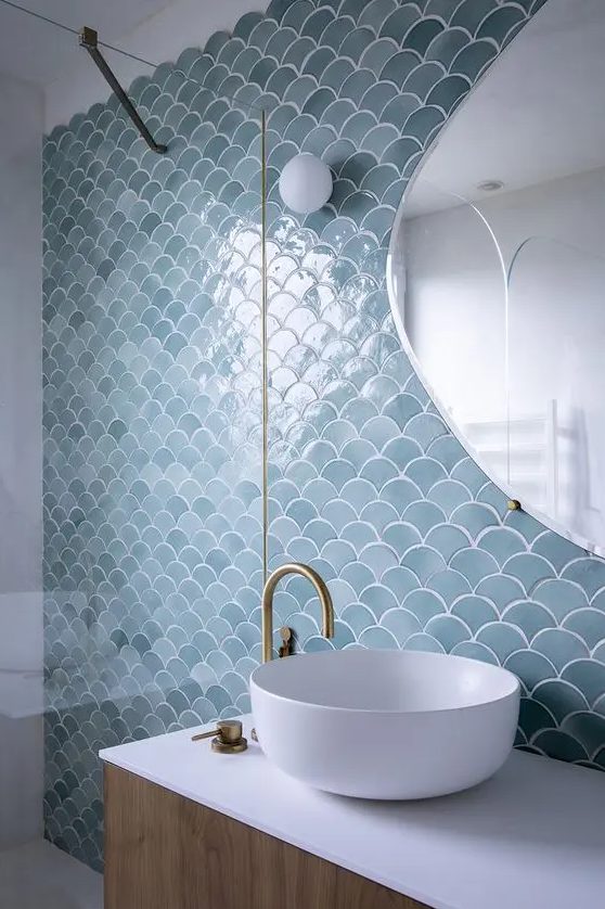 an accent wall done with blue fishscale tiles for an ocean feel in the bathroom, brass fixtures stand out in the backdrop