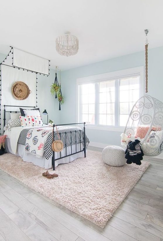 an airy boho teen girl bedroom with light blue walls, a bed with a cnaopy, printed bedding, a suspended chair and a blush rug