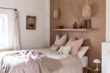an earthy bedroom with a terracotta wall, a bed with neutral bedding, a shelf with some decor and a bold printed rug