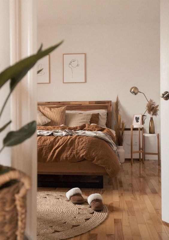 an earthy boho bedroom with a stained bed and rust bedding, side tables, a jute rug and some artwork is amazing