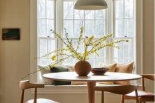 an earthy dining room with a bay window with a window seat, a round table and mid-century modern chairs, a pendant lamp