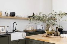 an earthy kitchen with dark green shaker cabinets and a matching kitchen island, black and butcherblock countertops, an open shelf and black fixtures