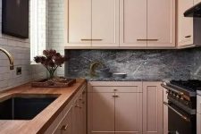 an eclectic kitchen with peachy pink cabinets, a white tile wall, a grey marble backsplash and dark appliances