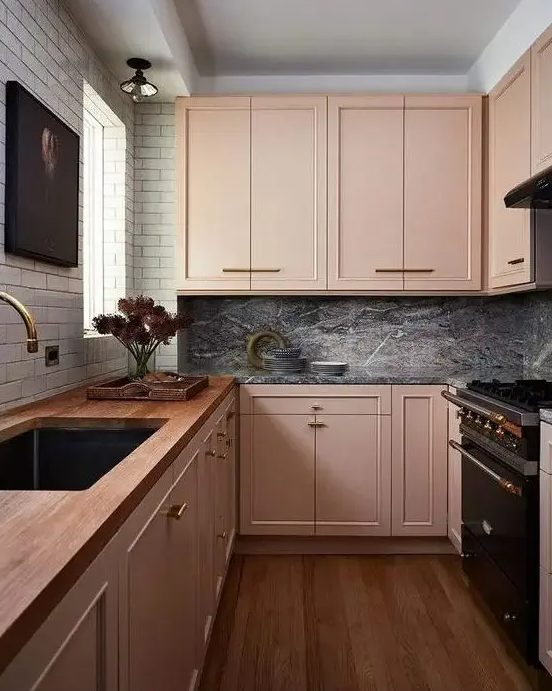 an eclectic kitchen with peachy pink cabinets, a white tile wall, a grey marble backsplash and dark appliances