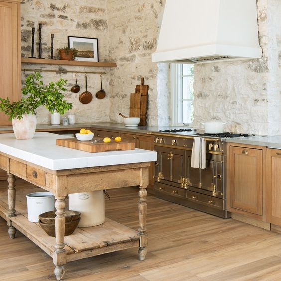 An eclectic kitchen with stone walls, light stained cabinets, a vintage cooker and a statement hood plus a vintage kitchen island