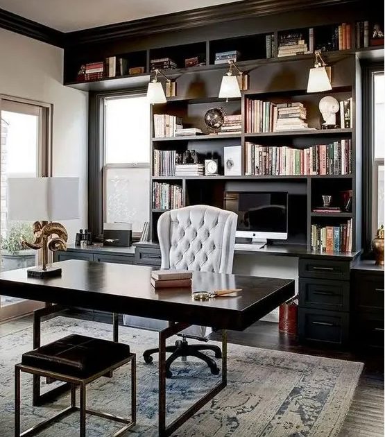 An elegant and chic masculine home office with a wooden desk and a stool, a built in bookcase and much natural ligjt