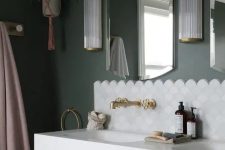 an elegant bathroom with green walls, a blush vanity, a sink, a white scallop tile accent, brass and gold fixtures