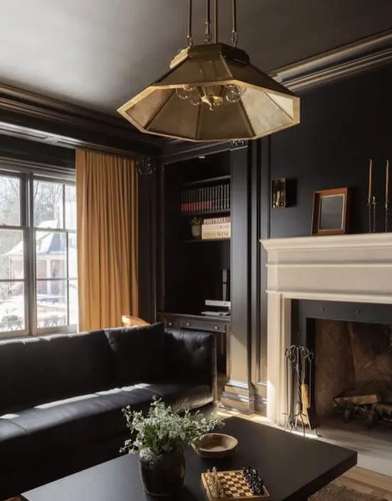 an elegant soot living room with a fireplace, a black leather sofa, built-in shelves, a coffee table and a chic pendant lamp