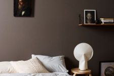 an exquisite bedroom with brown walls, a bed with neutral bedding, some art and a stool as a nightstand
