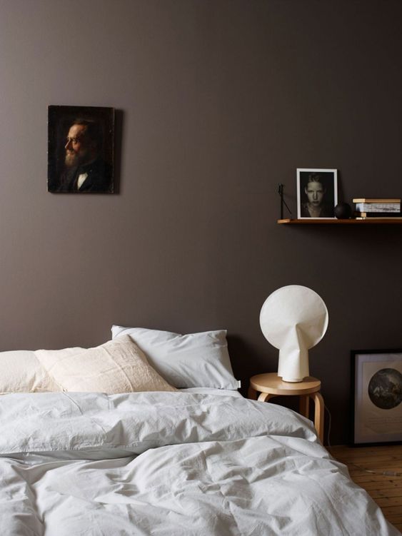 an exquisite bedroom with brown walls, a bed with neutral bedding, some art and a stool as a nightstand